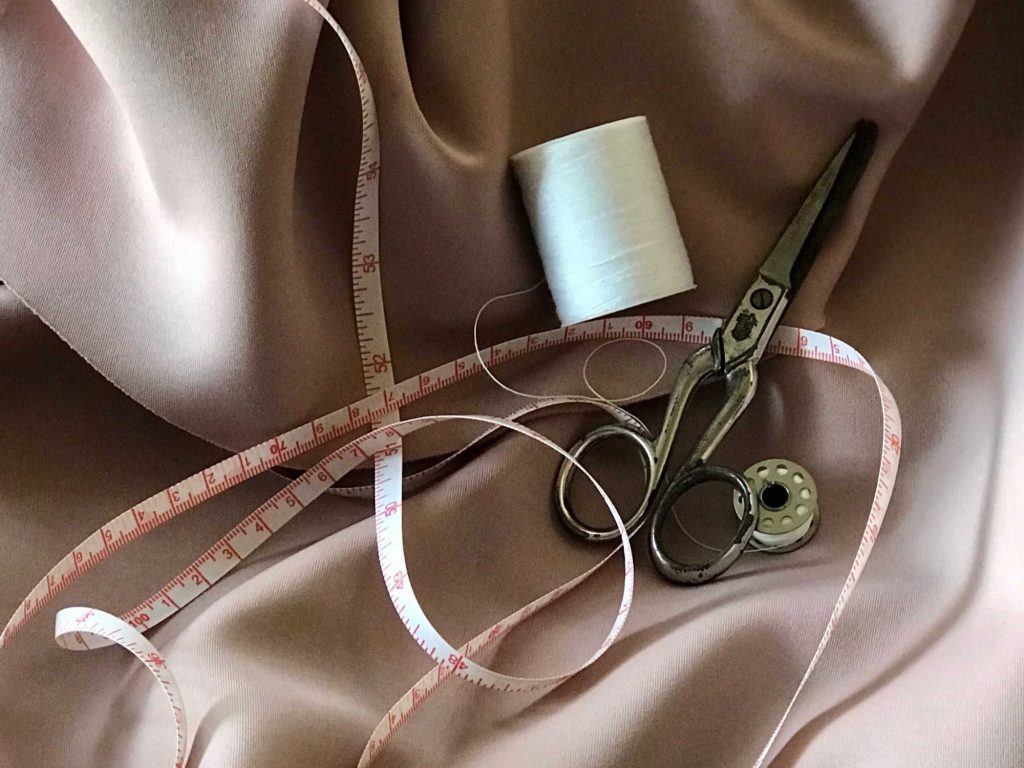 image of scissors, measuring tape and thread on fabric
