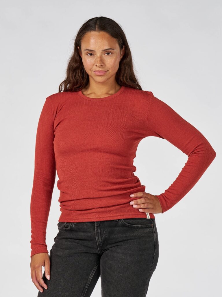 Person with long dark hair wearing a red merino base layer from Dilling and black jeans.