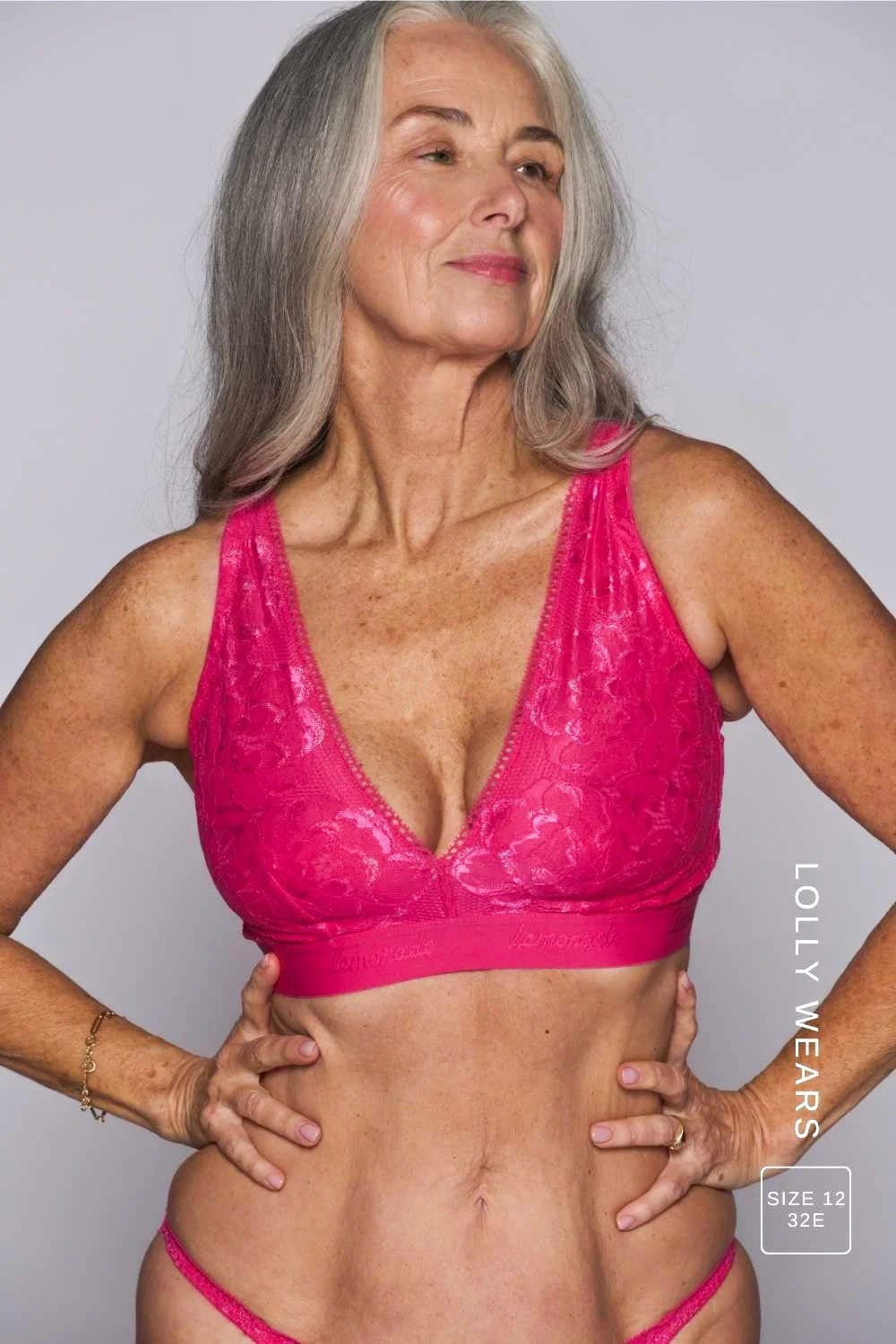 Smiling person with long grey hair wearing a bright pink bra from Lemonade Dolls